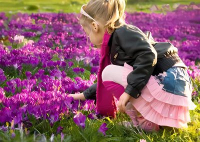 ein blondes Mädchen mit Zopf, Sonnenbrille und rosa Rock und Strümpfen kniet vor einem violetten Krokusblütenmeer am Blauen Band in Düsseldorf