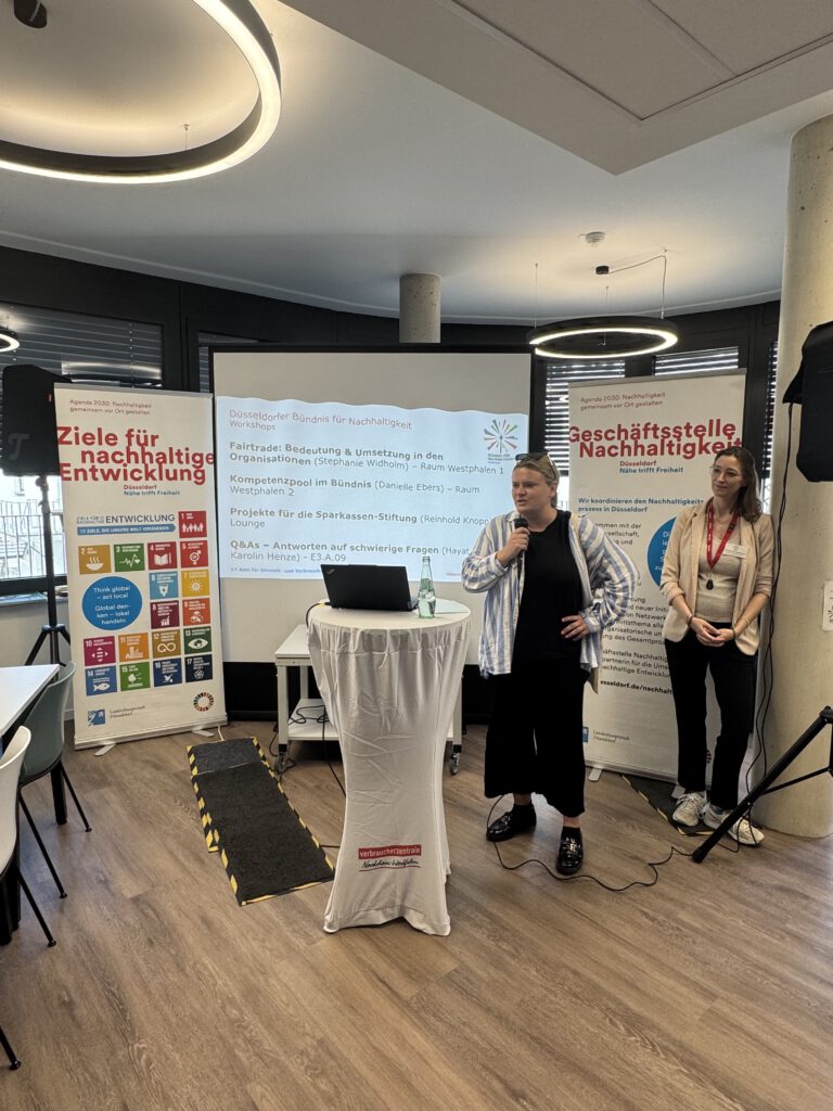 Jubiläumstreffen des Düsseldorfer Bündnisses für Nachhaltigkeit in der Verbraucherzentrale NRW Düsseldorf: Vortrag vor Workshop-Agenda, Banner zu SDGs und Geschäftsstelle Nachhaltigkeit.